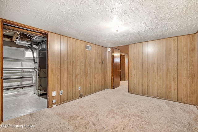 finished below grade area with wooden walls, visible vents, and a textured ceiling