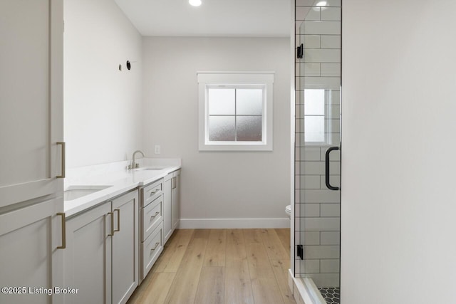 full bath with a shower stall, wood finished floors, a sink, double vanity, and baseboards