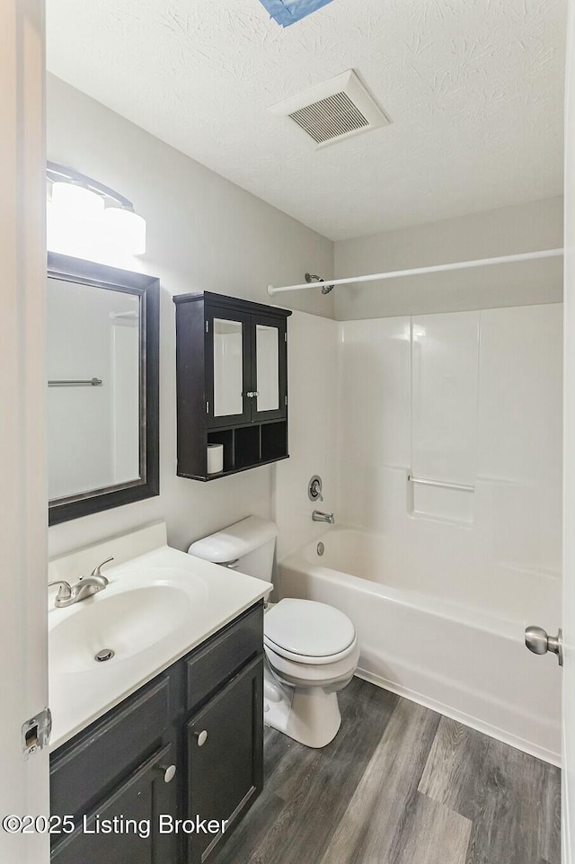 full bath featuring a textured ceiling, vanity, visible vents, toilet, and wood finished floors