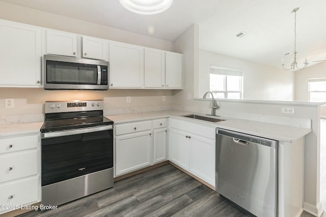 kitchen with a peninsula, light countertops, white cabinets, appliances with stainless steel finishes, and a sink