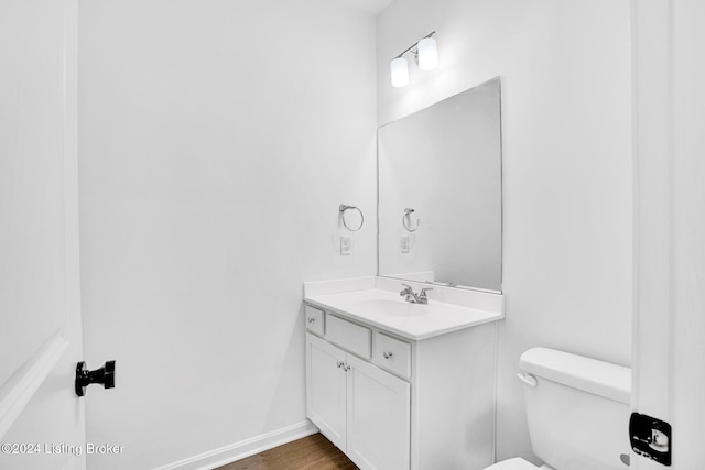 half bathroom with vanity, baseboards, toilet, and wood finished floors