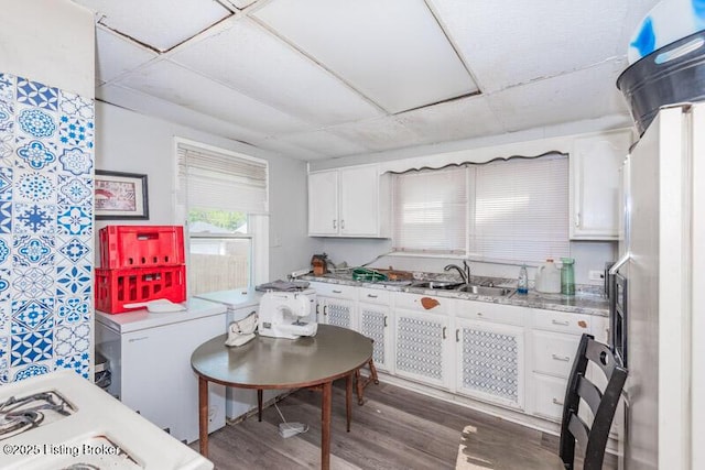 kitchen with a paneled ceiling, a sink, freestanding refrigerator, white cabinetry, and wood finished floors