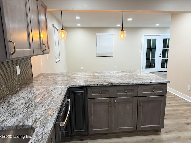 kitchen featuring a peninsula, light wood-type flooring, recessed lighting, decorative backsplash, and light stone countertops