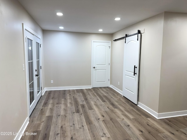 empty room featuring baseboards, wood finished floors, recessed lighting, and a barn door