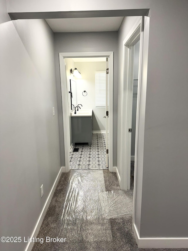 hallway with baseboards, a sink, and carpet flooring