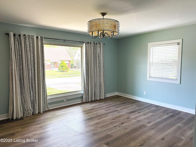 unfurnished room featuring wood finished floors, visible vents, baseboards, and an inviting chandelier
