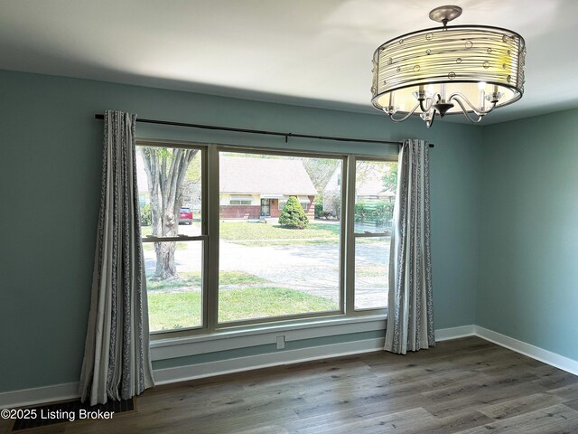 unfurnished dining area with a chandelier, wood finished floors, and baseboards