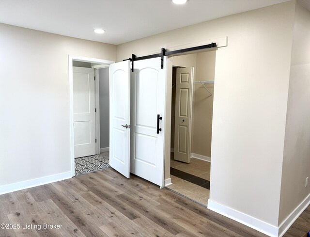 unfurnished bedroom featuring a barn door, wood finished floors, a walk in closet, baseboards, and recessed lighting