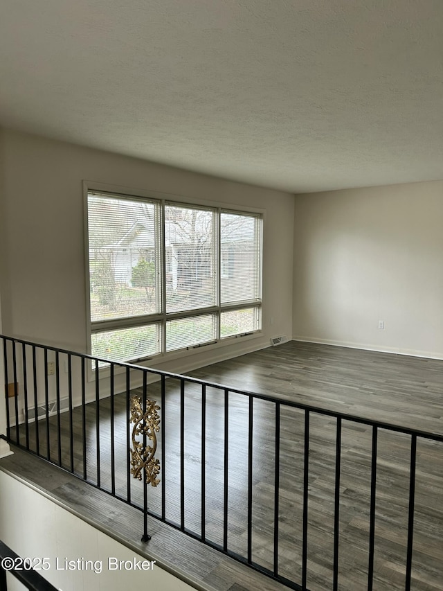 spare room featuring baseboards, wood finished floors, visible vents, and a textured ceiling