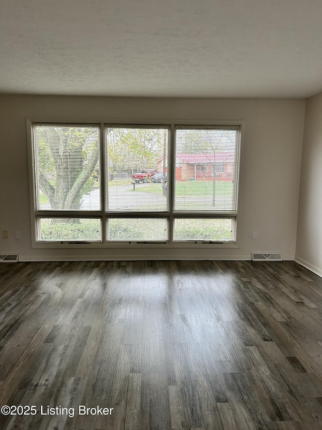 unfurnished room featuring dark wood-type flooring, visible vents, and a healthy amount of sunlight