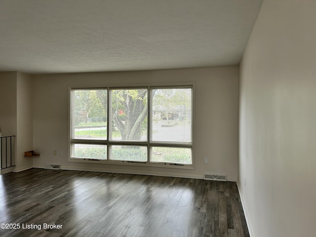 unfurnished room with baseboards, visible vents, a textured ceiling, and dark wood finished floors