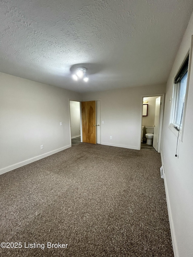 unfurnished bedroom with ensuite bath, a textured ceiling, carpet flooring, and baseboards