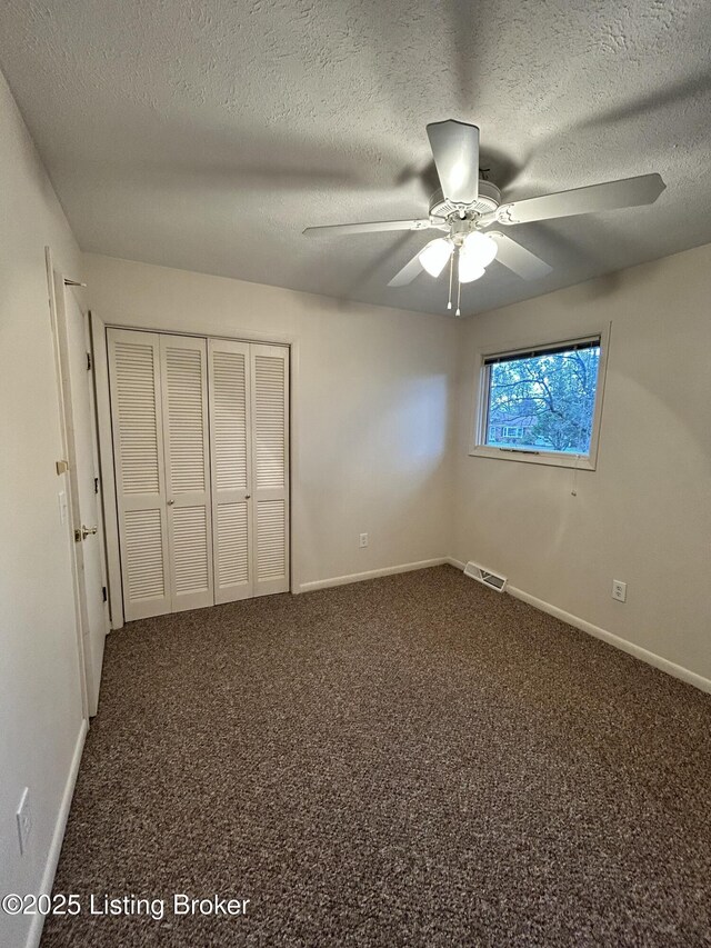 unfurnished bedroom with dark carpet, a textured ceiling, and a closet