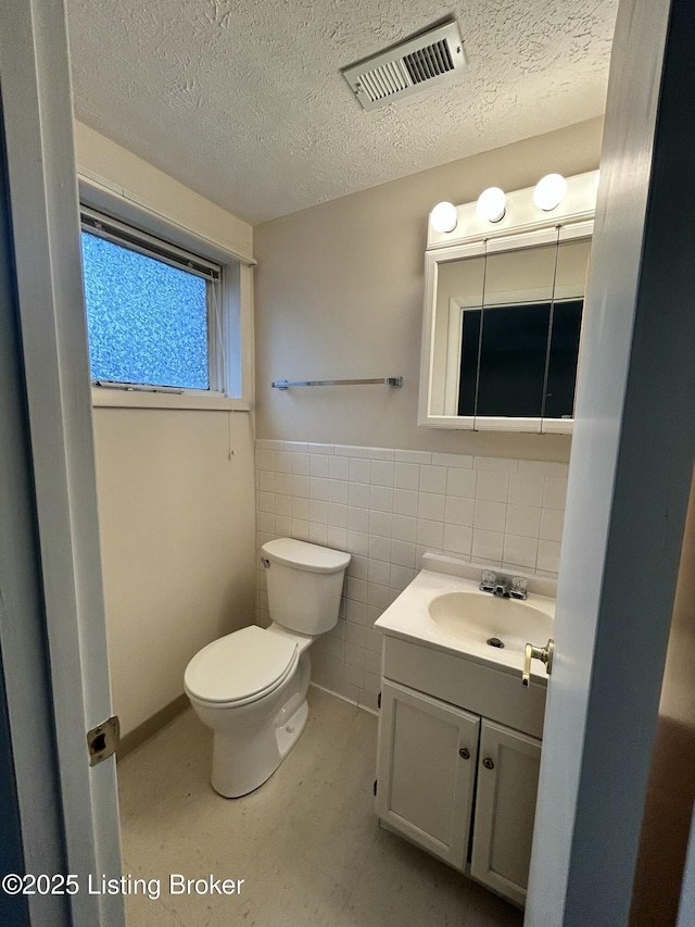 half bathroom featuring toilet, vanity, a textured ceiling, and visible vents