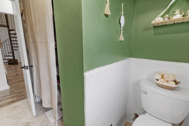 bathroom featuring toilet, a wainscoted wall, wood finished floors, and tile walls