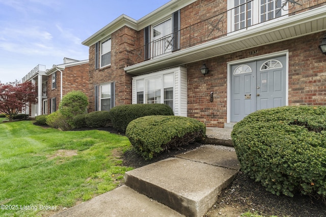 property entrance featuring brick siding, a yard, and a balcony