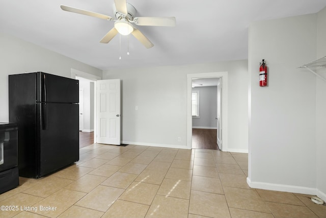 interior space featuring freestanding refrigerator, baseboards, ceiling fan, and light tile patterned floors