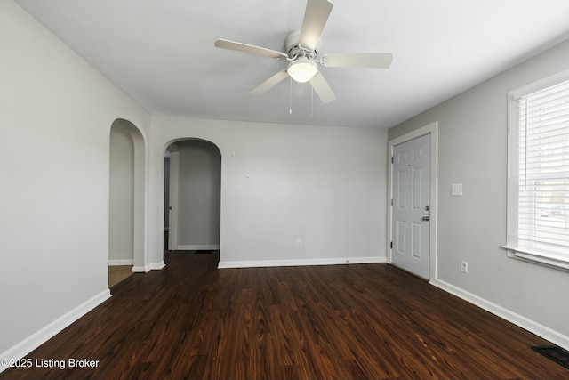 empty room featuring visible vents, a ceiling fan, wood finished floors, and arched walkways