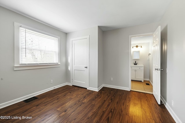 unfurnished bedroom featuring baseboards, dark wood-type flooring, visible vents, and ensuite bathroom