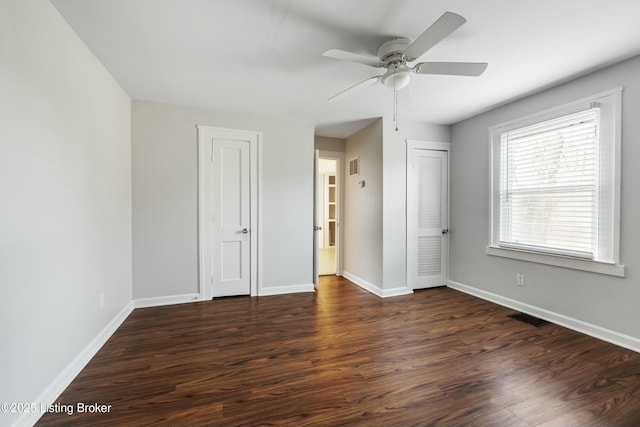 unfurnished room featuring dark wood finished floors, visible vents, a ceiling fan, and baseboards