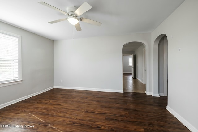 unfurnished room with arched walkways, wood finished floors, a ceiling fan, and baseboards