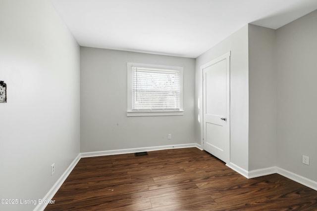 empty room featuring baseboards, visible vents, and dark wood-style floors