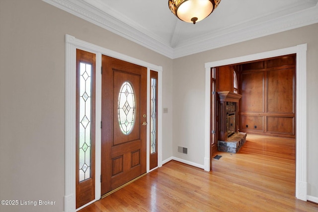entrance foyer featuring light wood finished floors, visible vents, crown molding, baseboards, and a glass covered fireplace