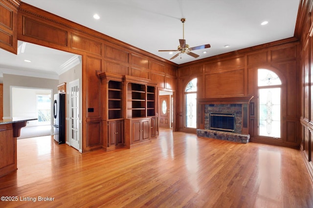 unfurnished living room with light wood-type flooring, ceiling fan, ornamental molding, and a decorative wall