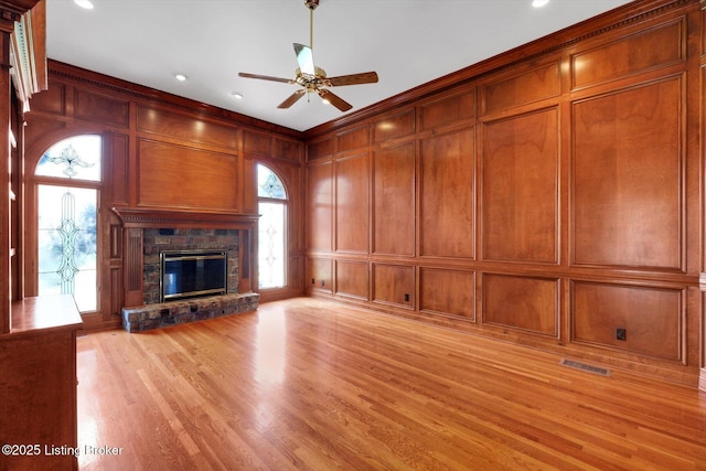 unfurnished living room with visible vents, light wood-style floors, a ceiling fan, a decorative wall, and a fireplace