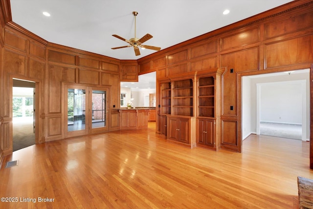 unfurnished living room with light wood-style flooring, visible vents, ceiling fan, and a decorative wall
