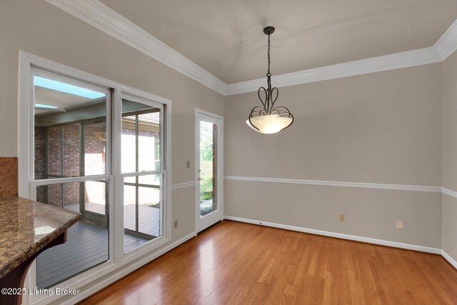 unfurnished dining area featuring wood finished floors, crown molding, and baseboards