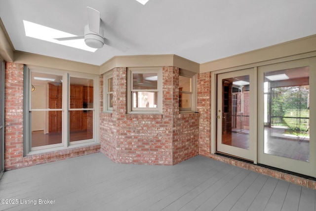 unfurnished sunroom with a skylight, brick wall, wood finished floors, and a deck