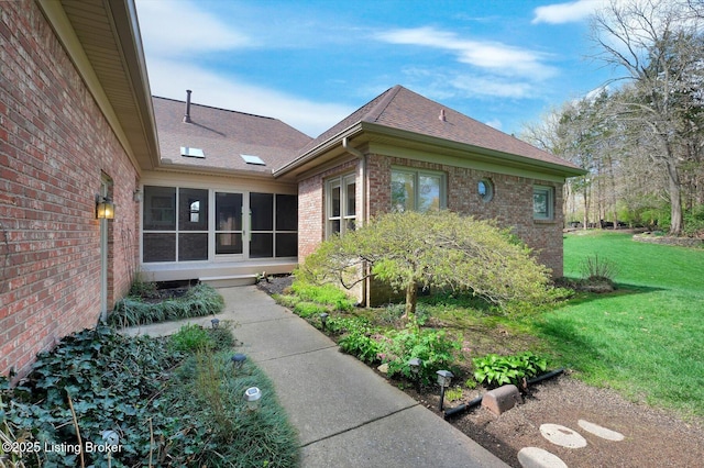 view of side of property with a yard, brick siding, roof with shingles, and a sunroom