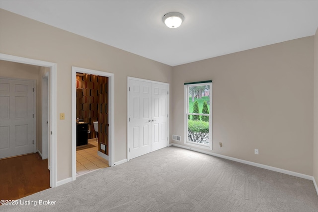unfurnished bedroom with light carpet, ensuite bathroom, visible vents, and baseboards