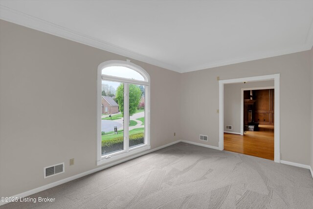 carpeted spare room with baseboards, ornamental molding, and visible vents