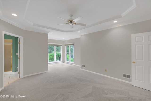 unfurnished room with a tray ceiling, visible vents, light carpet, ornamental molding, and ceiling fan