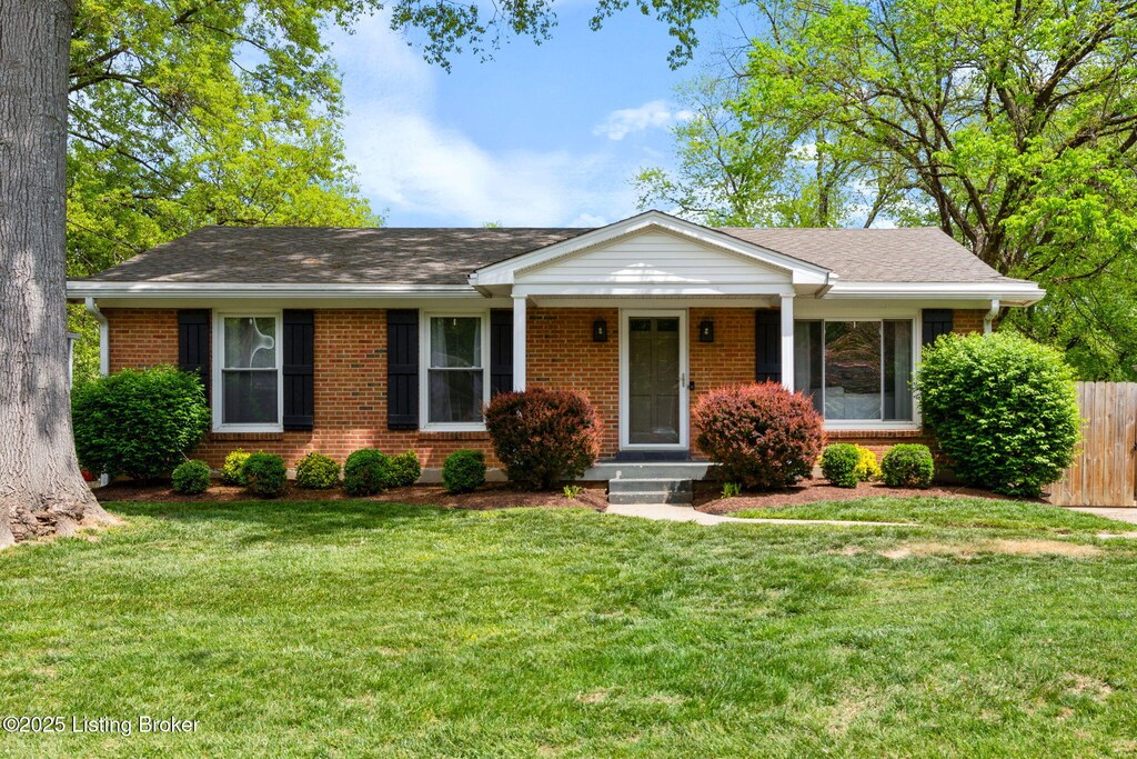 ranch-style house featuring fence, roof with shingles, a front yard, and brick siding