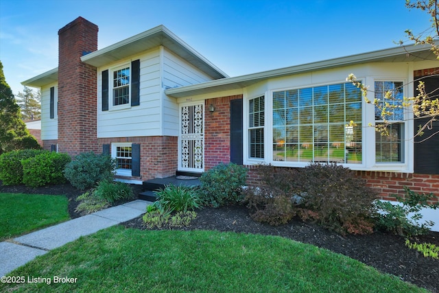 split level home featuring brick siding, a front lawn, and a chimney