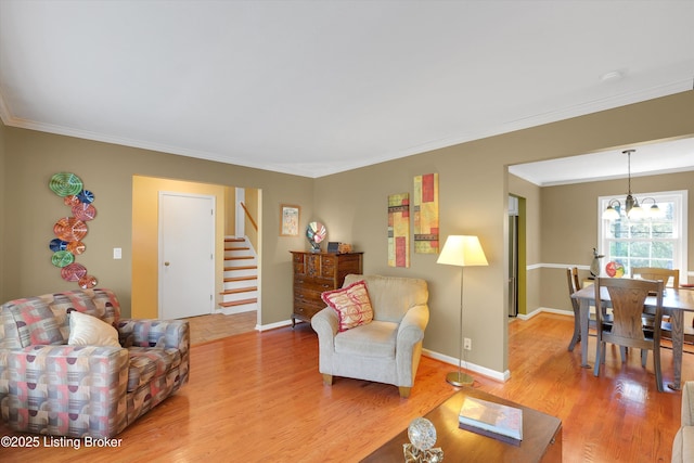 living room featuring light wood finished floors, baseboards, ornamental molding, and stairway