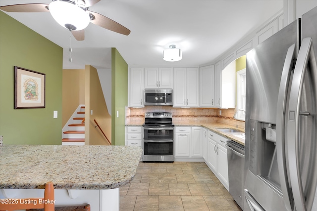 kitchen with stainless steel appliances, backsplash, white cabinetry, a sink, and ceiling fan
