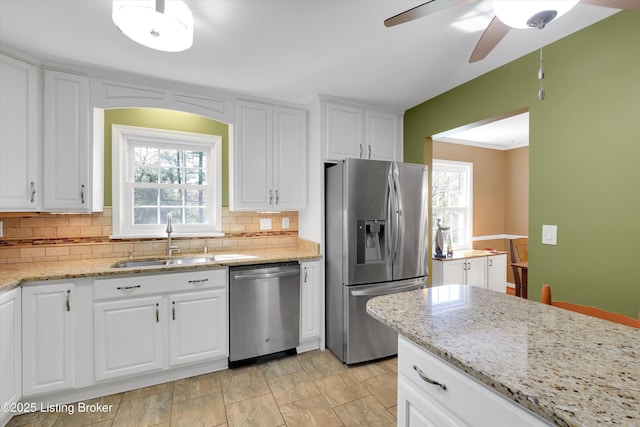 kitchen with backsplash, white cabinetry, a sink, appliances with stainless steel finishes, and ceiling fan