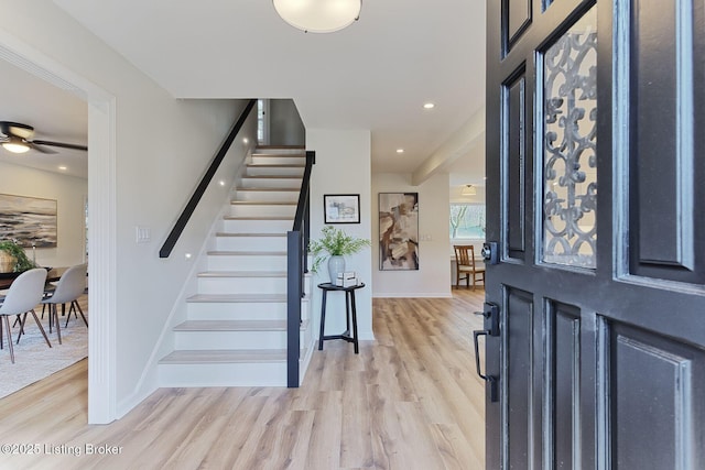 foyer featuring ceiling fan, light wood-type flooring, baseboards, and stairway