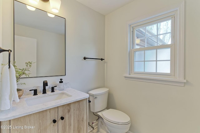half bath featuring baseboards, vanity, and toilet