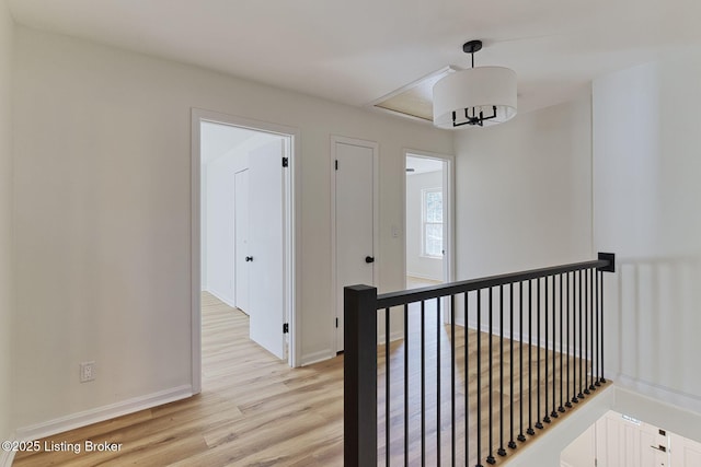 corridor with baseboards, an upstairs landing, and light wood finished floors