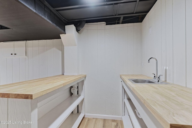 laundry area with wooden walls, baseboards, a sink, and light wood finished floors