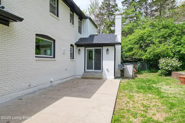 entrance to property with a chimney, fence, a patio, a lawn, and brick siding