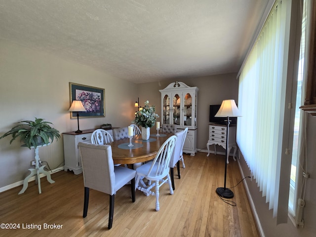dining space with light wood-style floors, a textured ceiling, and baseboards