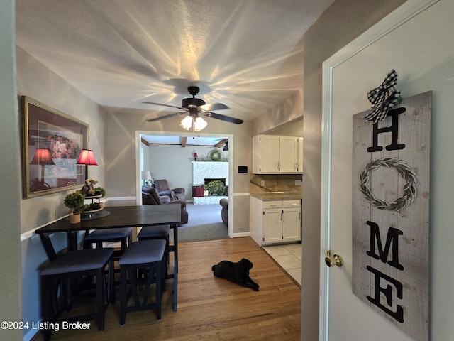 dining room with light wood finished floors, a ceiling fan, and a fireplace with raised hearth