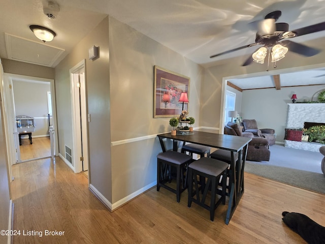 dining space with baseboards, a ceiling fan, a fireplace with raised hearth, and light wood-type flooring
