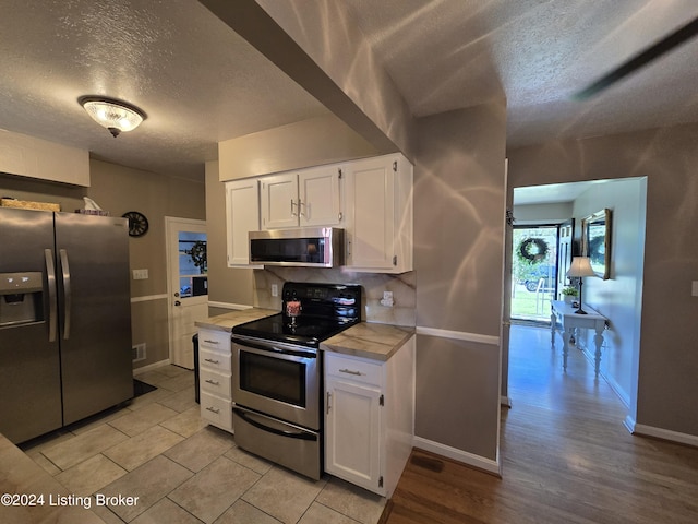 kitchen featuring white cabinets, a textured ceiling, baseboards, and stainless steel appliances